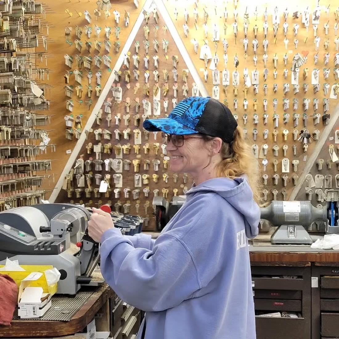 A Central Key & Safe locksmith cutting a key in front of the shop's wall of key blanks
